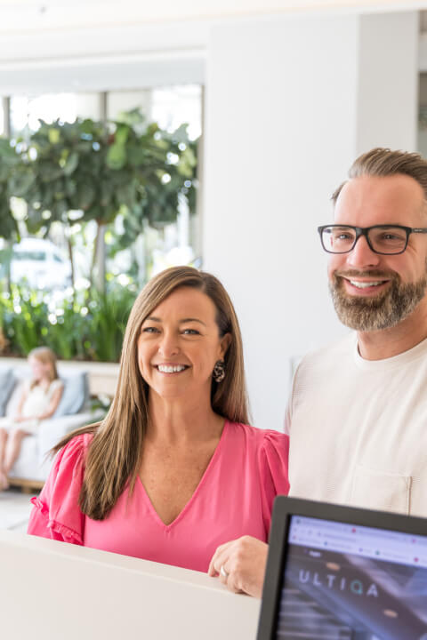 Couple smiling while checking in at the ULTIQA resort reception desk, greeted by a staff member.