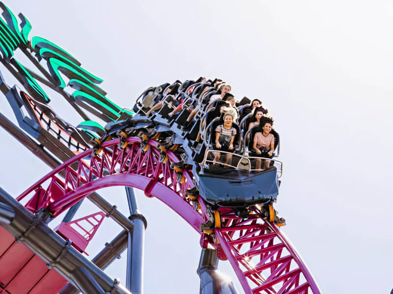 People riding a high-speed roller coaster with bright pink and black tracks at a Gold Coast theme park.