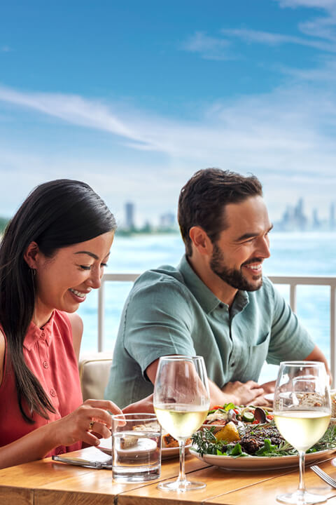 Four people at the table enjoying sandwitches and laughing with the view of Gold Coast in the background.