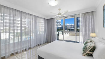 Main bedroom at ULTIQA Beach Haven on Broadbeach with a queen bed, bedside lamp, ceiling fan, and sliding doors opening to the balcony.