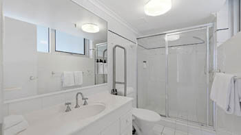 Bathroom at ULTIQA Beach Haven on Broadbeach with vanity, large mirror, toilet, and glass-enclosed shower.