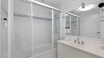 Bathroom at ULTIQA Beach Haven on Broadbeach featuring a bathtub with glass screen, vanity, mirror, and tiled finishes.