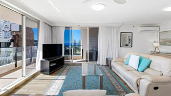 Bright lounge at ULTIQA Beach Haven on Broadbeach with TV, balcony access, and coastal outlook visible beyond the buildings.