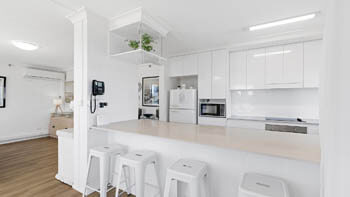 Modern white kitchen at ULTIQA Beach Haven on Broadbeach with a large island bench, bar stools, and clean contemporary finishes.