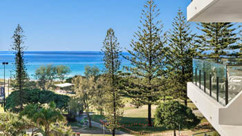 Elevated view over parkland and tall pines to the turquoise ocean and beach, seen from the balcony at ULTIQA Beach Haven on Broadbeach.