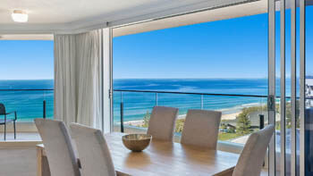 Wooden table with 7 chairs and ocean views in the background at ULTIQA Beach Haven on Broadbeach.