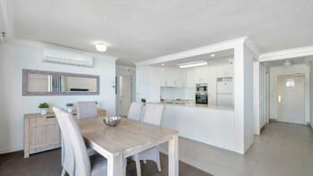Dining area and kitchen in the background with clean white walls at ULTIQA Beach Haven on Broadbeach.