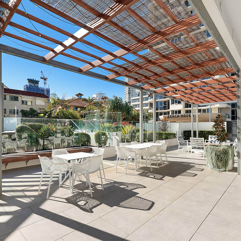 Outdoor swimming pool and spa area at ULTIQA Points North Coolangatta, surrounded by sun loungers, palm trees, and high-rise buildings under a bright blue sky.